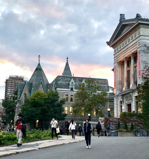 About a dozen students walk outdoors on the McGill campus in front of university buildings.